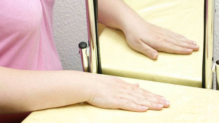 Patienten betrachtet Hand im Spiegel bei der Spiegeltherapie