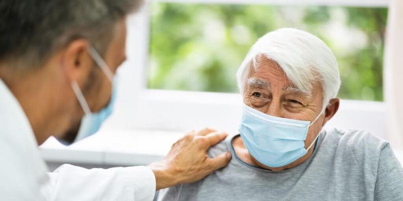 Arzt mit Mundschutz spricht mit älterem Patienten mit Mundschutz