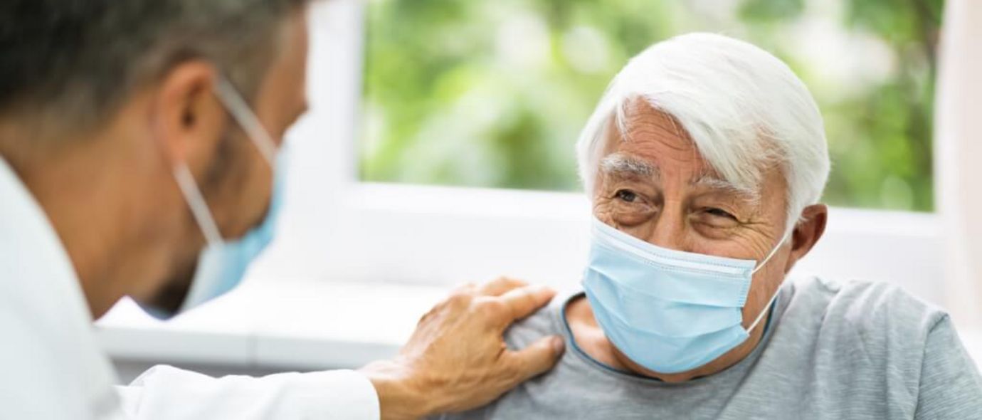 Arzt mit Mundschutz spricht mit älterem Patienten mit Mundschutz
