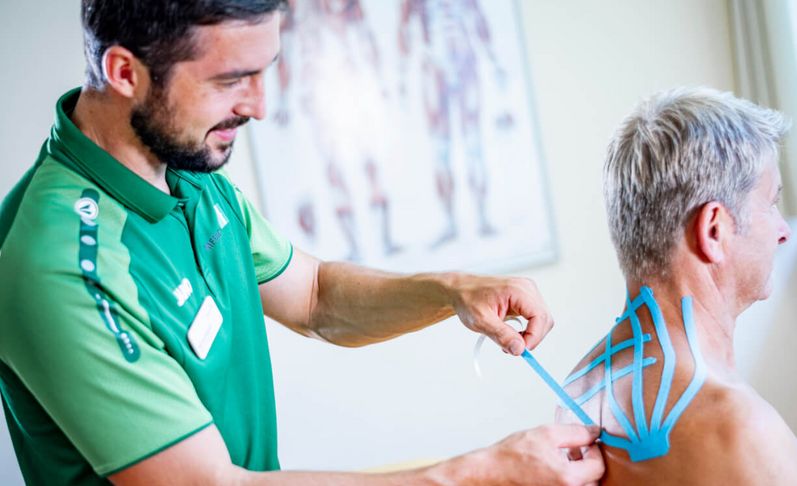 Therapeut klebt Patienten Kinesiotape auf den Rücken