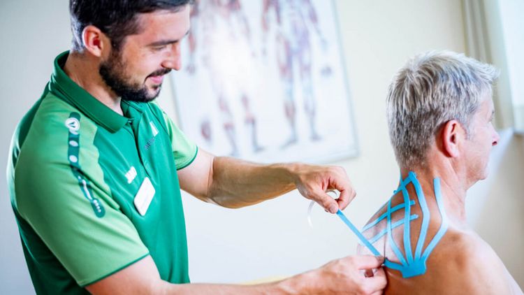 Therapeut klebt Patienten Kinesiotape auf den Rücken