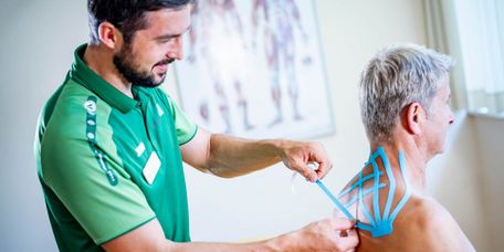 Kinesiotaping Therapeut klebt Patienten Kinesiotape auf den Rücken