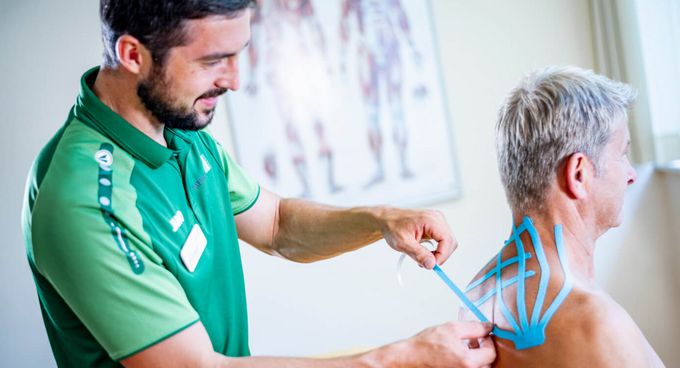 Therapeut klebt Patienten Kinesiotape auf den Rücken