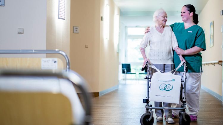 Pflegekraft begleitet ältere Patientin durch den Flur