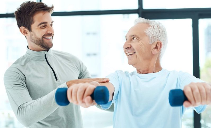 Therapeut unterstützt älteren männlichen Patienten beim Hanteltraining